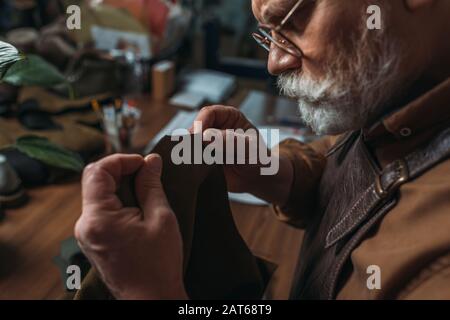 Aufmerksamer, leitender Schuhmacher, der in der Werkstatt echtes Leder hält Stockfoto