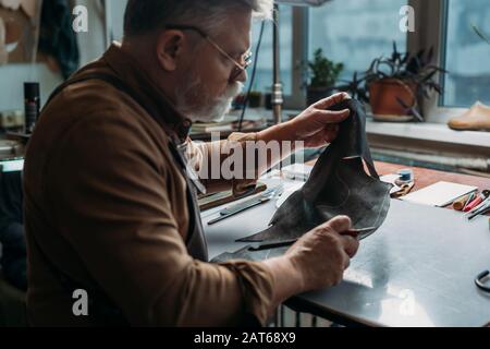 Leitender Schuhmacher, der in der Werkstatt Originalleder hält Stockfoto