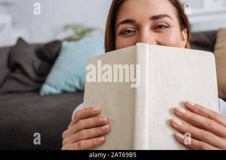 Selektiver Fokus der jungen Frau, die Gesicht mit Buch bedeckt Stockfoto