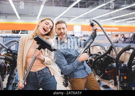 Freund, der mit Staubsauger und Freundin im Haushaltsgerätgeschäft singt Stockfoto