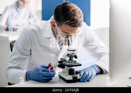 Genetisches Beratungsunternehmen, das Reagenzgläser hält und Mikroskop im Labor verwendet Stockfoto