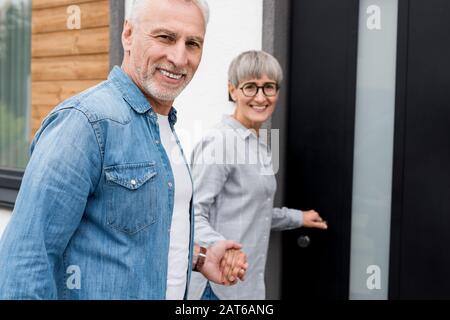 Lächelnde Frau, die die Hände mit dem Mann hält und in ein neues Haus eindringt Stockfoto