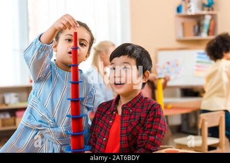 Selektiver Fokus von Kindern, die mit Lehrer und Kind im Hintergrund in der montessori-klasse ein pädagogisches Spiel spielen Stockfoto