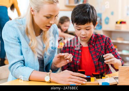 Selektiver Fokus von Lehrer und Kind, die Bausteine mit Kindern im Hintergrund in der montessori-schule spielen Stockfoto