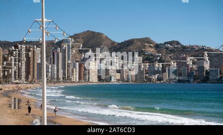 Touristen, die am Strand Playa de Levante mit Wolkenkratzern von Rincón de Loix und dem Naturpark Serra Gelada auf der Rückseite spazieren gehen (Benidorm, Alicante, Spanien) Stockfoto