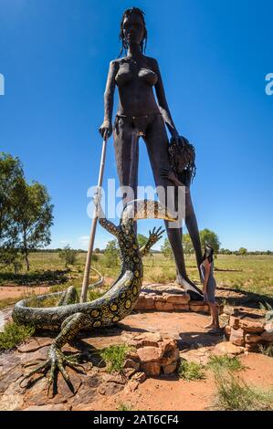 Eine Besucherin, die ein Gefühl von Ausmaßung gibt, während sie die Statue einer Mutter, eines Kindes und einer Goanna von Anmatjere bei Einem Querruder im Northern Territory bewundert. Stockfoto