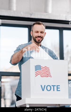 Glückliche bärtige Männer wählen und Wahlzettel mit Wahlschrift in die Box legen Stockfoto