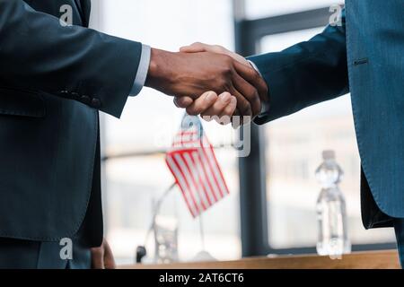 Ein verschneiter Blick auf multikulturelle Diplomaten, die die Hände in der Nähe der Flagge amerikas schütteln Stockfoto