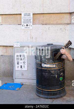 Straßenbuscher versteckt sich in Mülltonne und spielt Gitarre in Cambridge, Großbritannien Stockfoto