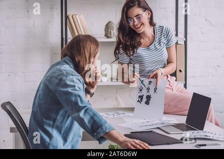 Selektive Fokussierung des fröhlichen Illustrators, der Cartoon-Skizzen in der Nähe des Menschen hält Stockfoto