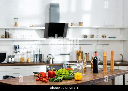 Gemüse: Flaschen mit Wein und Bier, Weingläser, Schüssel, Pfeffermühle, Salzmühle auf Holztisch in der Küche Stockfoto