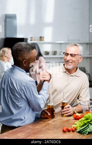 afroamerikanischer Mann hält die Hände und spricht mit lächelnden Freunden in der Küche Stockfoto