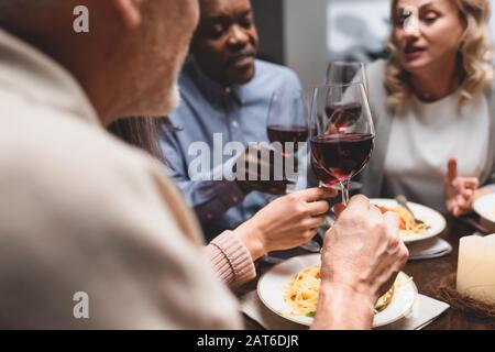 Blick auf multikulturelle Freunde, die während des Abendessens mit Weingläsern sprechen und halten Stockfoto