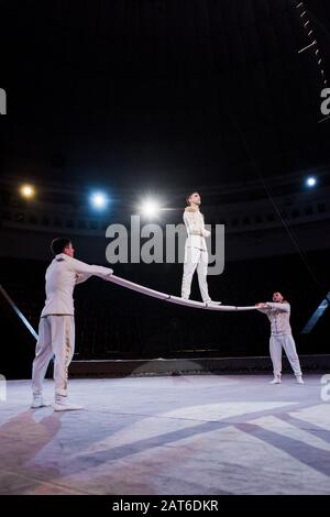 Turnerin steht auf der Stange in der Nähe von Akrobaten im Zirkus Stockfoto