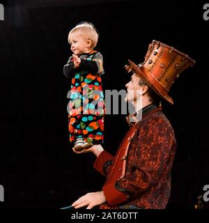 Glücklicher Mann, der niedliches Kleinkind in der Hand hält, während er im Zirkus auftrat Stockfoto