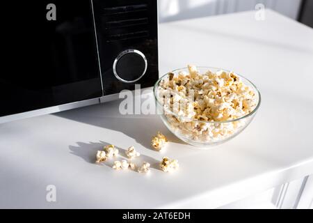 Popcorn in der Schüssel in der Nähe der Mikrowelle auf dem Tisch in der Küche Stockfoto