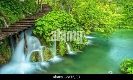 Eine lange Naturszene mit Wasserfällen, die unter einem Holzsteg in einem Wald im Plitvicer Lakes National Park in Kroatien fließen. Stockfoto