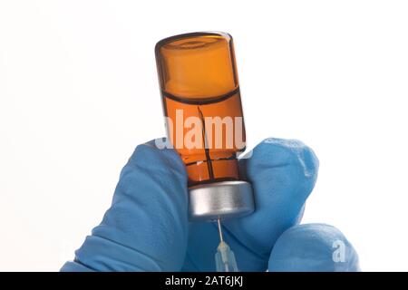 Die Spritze saugt flüssige Medikamente aus der bernsteinfarbenen Durchstechflasche in der Hand der Pflegekraft mit Handschuhen. Stockfoto