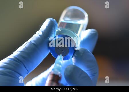 Die Spritze saugt flüssige Medikamente aus der blau gefärbten Durchstechflasche in der Hand der Pflegekraft mit Handschuhen. Stockfoto