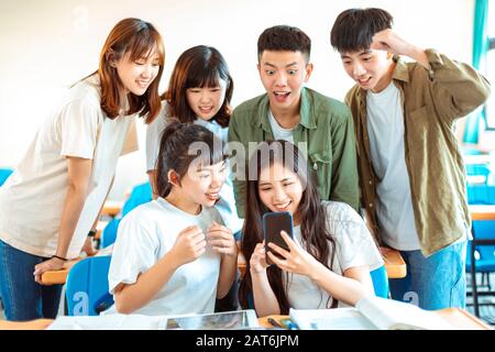 Fröhliche Studenten, die Smartphones im Klassenzimmer betrachten Stockfoto