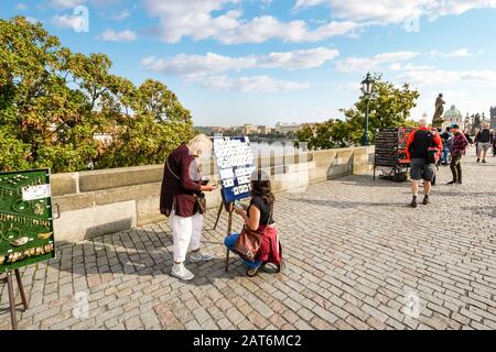 Eine Frau kauft lokale Souvenirs von einem Straßenhändler auf der Karlsbrücke in Prag, Tschechien Stockfoto