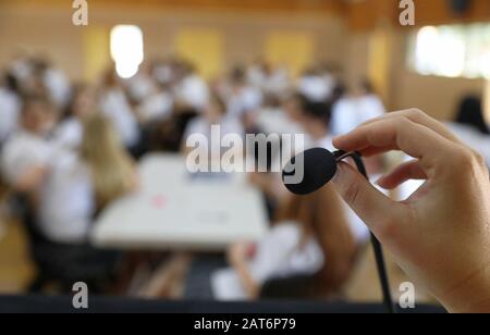 Ein Sichtbild einer Hand und Finger, die ein Mikrofon halten und einstellen, während sie in der Öffentlichkeit vor einem Publikum in einem Saal sprechen Stockfoto