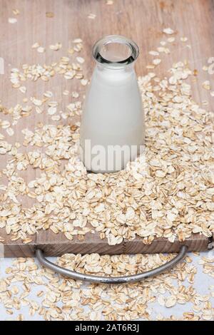 Vegane pflanzenbasierte Milchalternativen. Hafermilch und Hafer auf einem Holzbrett Stockfoto