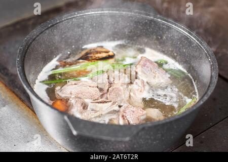 Traditionelle Rinderbrühe mit Gemüse, Knochen und Zutaten im Topf, Kochrezept. Suppe in einem Kochtopf mit Pfanne auf dunklem Steingrund. Oben Stockfoto