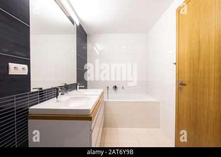 Modernes Badezimmer mit großem Spiegel und zwei Waschbecken, Badewanne und Holztür Stockfoto