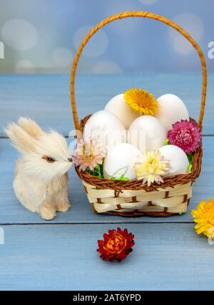 Der Osterhase sitzt neben einem Korb voller Eier, dekoriert mit getrockneten Blumen. Stockfoto