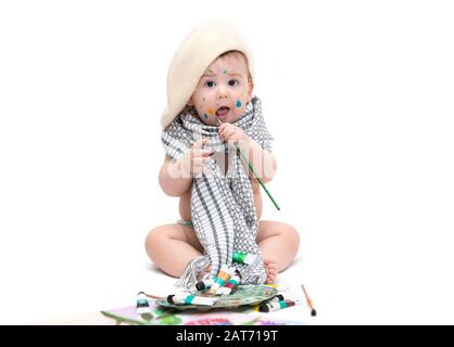 Kleines Künstlerbaby, das mit Farben sitzt, die auf Weiß isoliert sind Stockfoto