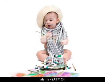 Kleines Künstlerbaby, das mit Farben sitzt, die auf Weiß isoliert sind Stockfoto