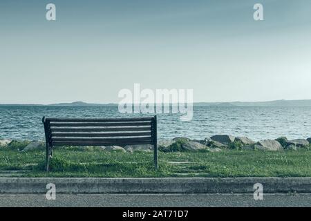 Einsame alte Holzbank an der Küste bei Sonnenuntergang, Konzept gebleichtes Foto Stockfoto