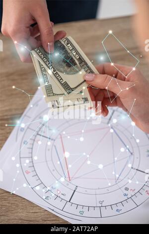 Beschnittenes Bild des Mannes, der dem Astrologen neben Geburtshoroskop und Sternbildern Bargeld gibt Stockfoto