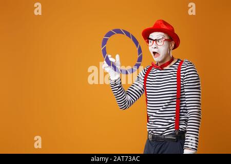 Clown MIME mit blauem Ring auf leerem orangefarbenem Hintergrund Stockfoto