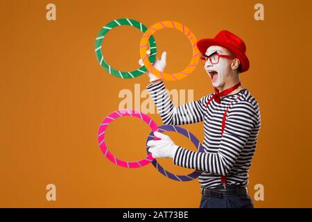 Fröhlicher MIME mit mehrfarbigen Ringen auf leerem orangefarbenem Hintergrund Stockfoto