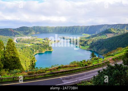 Wundervolle Aussicht auf die Seen Sete Cidades, fotografiert vom Aussichtspunkt Vista do Rei auf der Insel San Miguel, den Azoren, Portugal. Blauer Vulkansee umgeben von grünem Wald. Straße im Vordergrund. Stockfoto