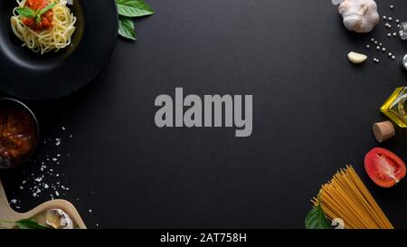 Overhead-Aufnahme von Zutaten klassischer italienischer Spaghetti-Pasta mit Tomatensauce und Kopierraum auf dunklem Hintergrund Stockfoto