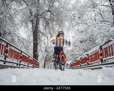 Der Junge fährt im Winter im Park mit dem Fahrrad unter den schneebedeckten Bäumen Stockfoto