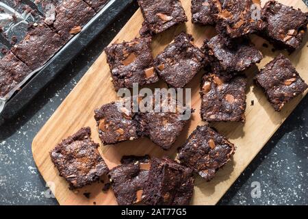 Schokoladenbrownie aus Backform herausgenommen und auf Holzbrett platziert - Draufsicht Foto Brownies mit geschmolzenen Schokoladenbits Stockfoto
