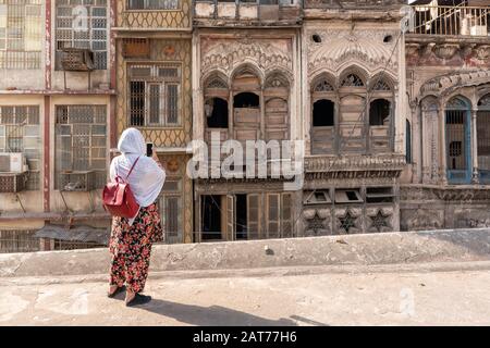 Pakistanisches Mädchen in Blumensalwar kameez mit dem Handy ein Foto von Holzfenstern in der Villa Haveli in Peschawar, Pakistan Stockfoto