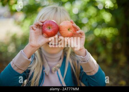 Portrait des Mädchens, das roten organischen apfel im Freien isst. Erntekonzept. Kind pflückt im Herbst Äpfel auf dem Bauernhof. Kinder und Ökologie. Gesunde Ernährung Ga Stockfoto