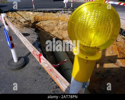 Straßenbarriere aus rot-weißen Holzbohlen auf Kunststoffpfosten mit bernsteinfarben gelben Rundwarnungen und Warnblinkleuchten. Dunkelgraue Asphaltoberfläche. Stockfoto