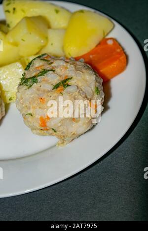 Fleischfleischbällchen mit gekochten Kartoffeln und gekochten Karotten auf einem weißen Teller auf dunklem Hintergrund. Nahaufnahme Stockfoto