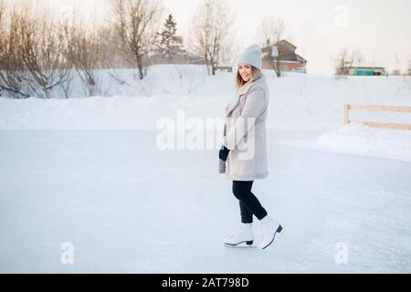 Schöne Frau auf weißem Eiskleider in warmer Kleidung und gestricktem Wollhut, blickt in den Rahmen und lächelt. Aktives Winterurlaubskonzept Stockfoto