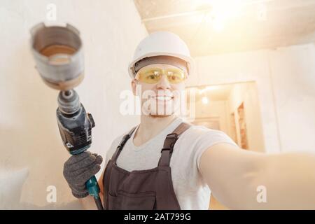 Bauarbeiter Mann macht selfie Foto mit Schutzbrille und weißem Helm mit pneumatischen Hammerbohrern Stockfoto