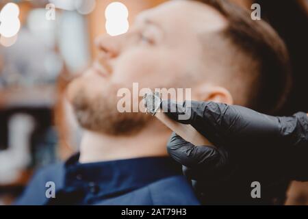 Master barber entfernt Haare aus der Nase des Menschen mit Wachs, Depilation Beauty Verfahren Stockfoto