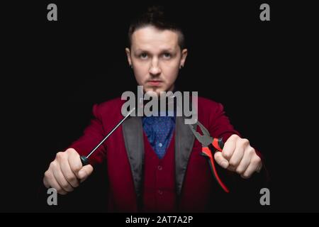 Der männliche Zauberer experimentiert mit Zauberstäben mit dem Schraubendreher-Werkzeug, schwarzer Hintergrund Stockfoto