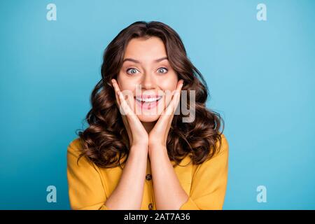 Closeup-Foto der attraktiven lockigen Dame hält Hände auf Wangenknochen überglücklich fröhliche Rabattpreise Zeitraum tragen Schalenbekleidung gelbes Hemd isoliert blau Stockfoto