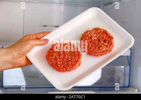 Roher Hühnchenburger im Behälter stehen im offenen Kühlschrank auf dem Regal. Zutat zum Kochen von Fleischgerichten. Unbehacktes Fleisch. Stockfoto